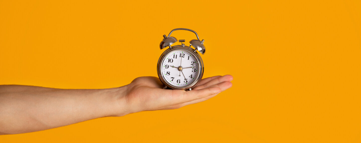 Time management and deadline. Millennial guy holding alarm clock over orange background, closeup