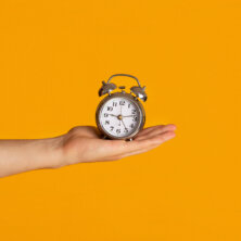 Time management and deadline. Millennial guy holding alarm clock over orange background, closeup